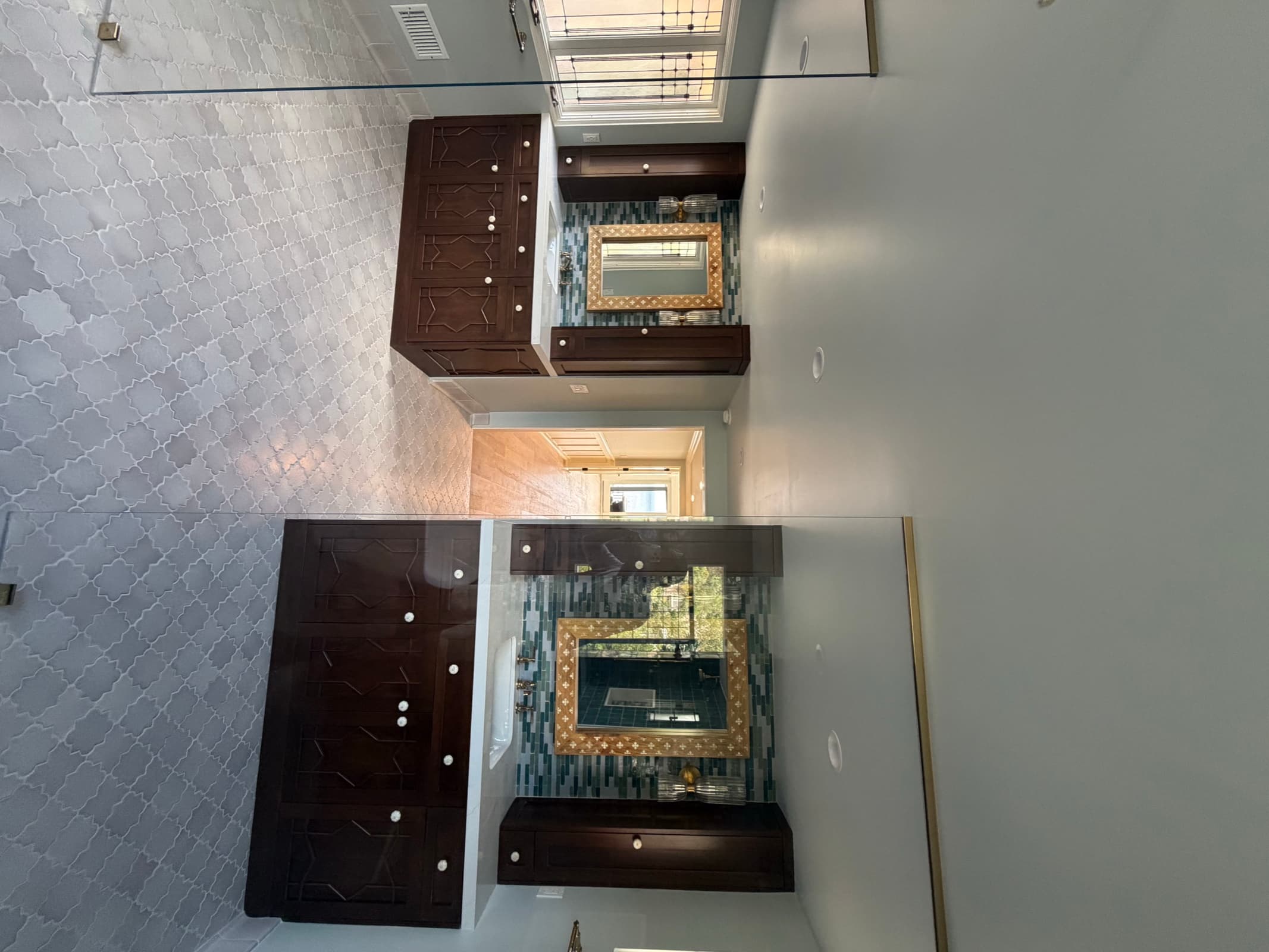Double vanities in carved dark wood with sea-glass tile and a glass wet-room partition, Laguna Niguel bathroom remodel