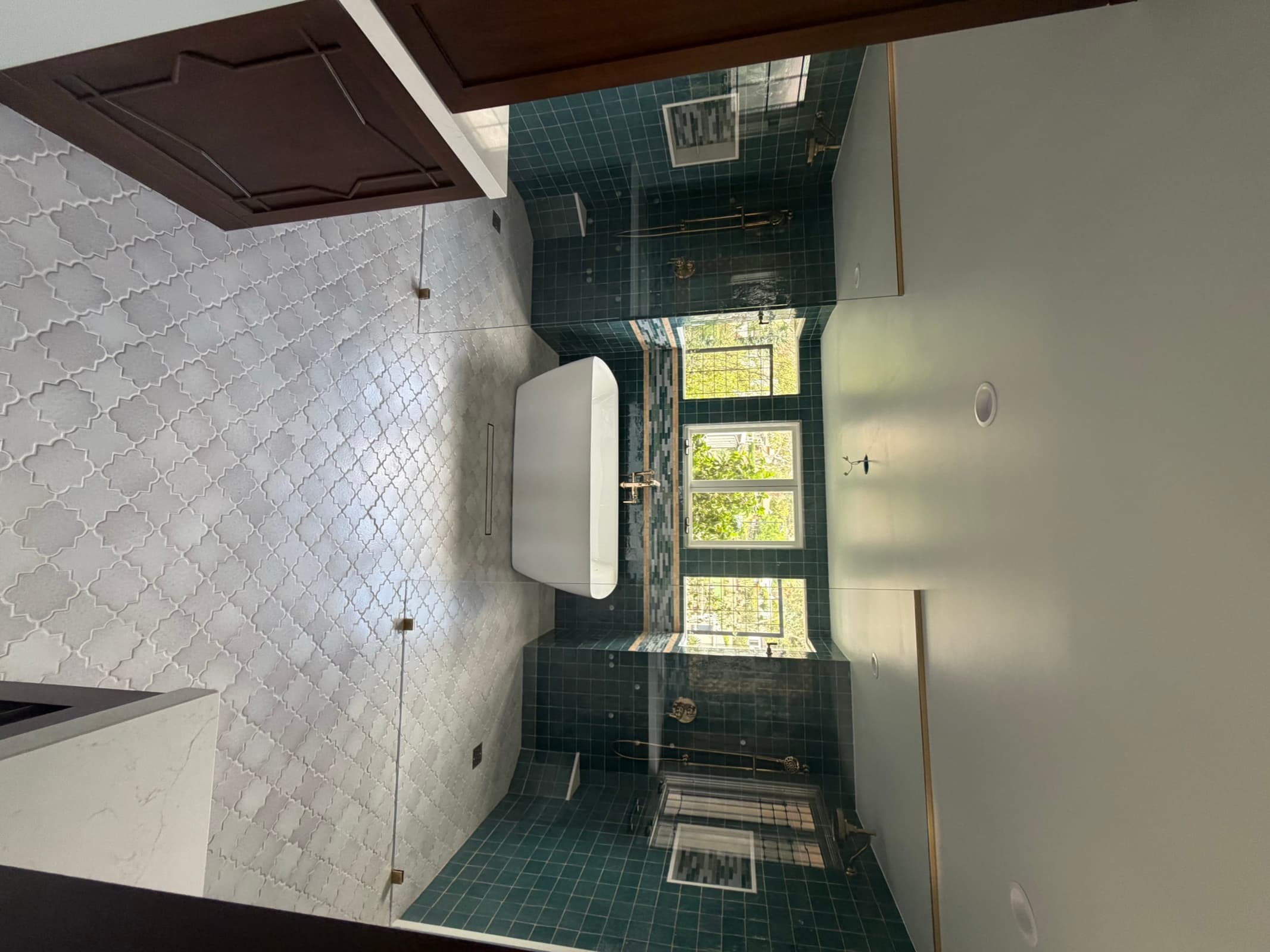 Freestanding tub against teal handmade-look tile with brass fixtures in the wet room