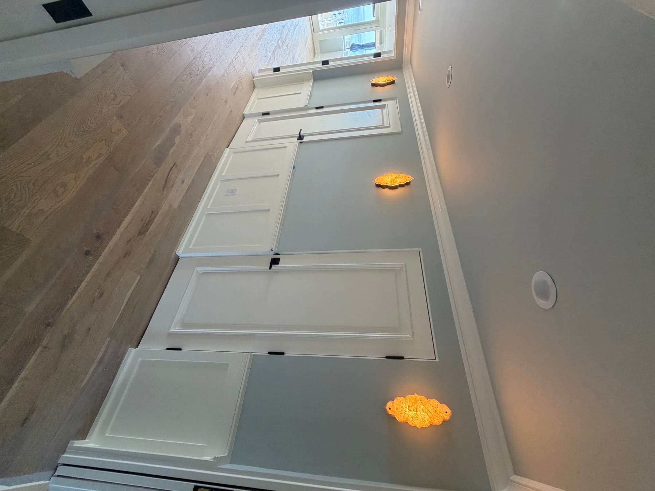 Dressing area with white paneled built-in wardrobes, amber sconces, and oak flooring