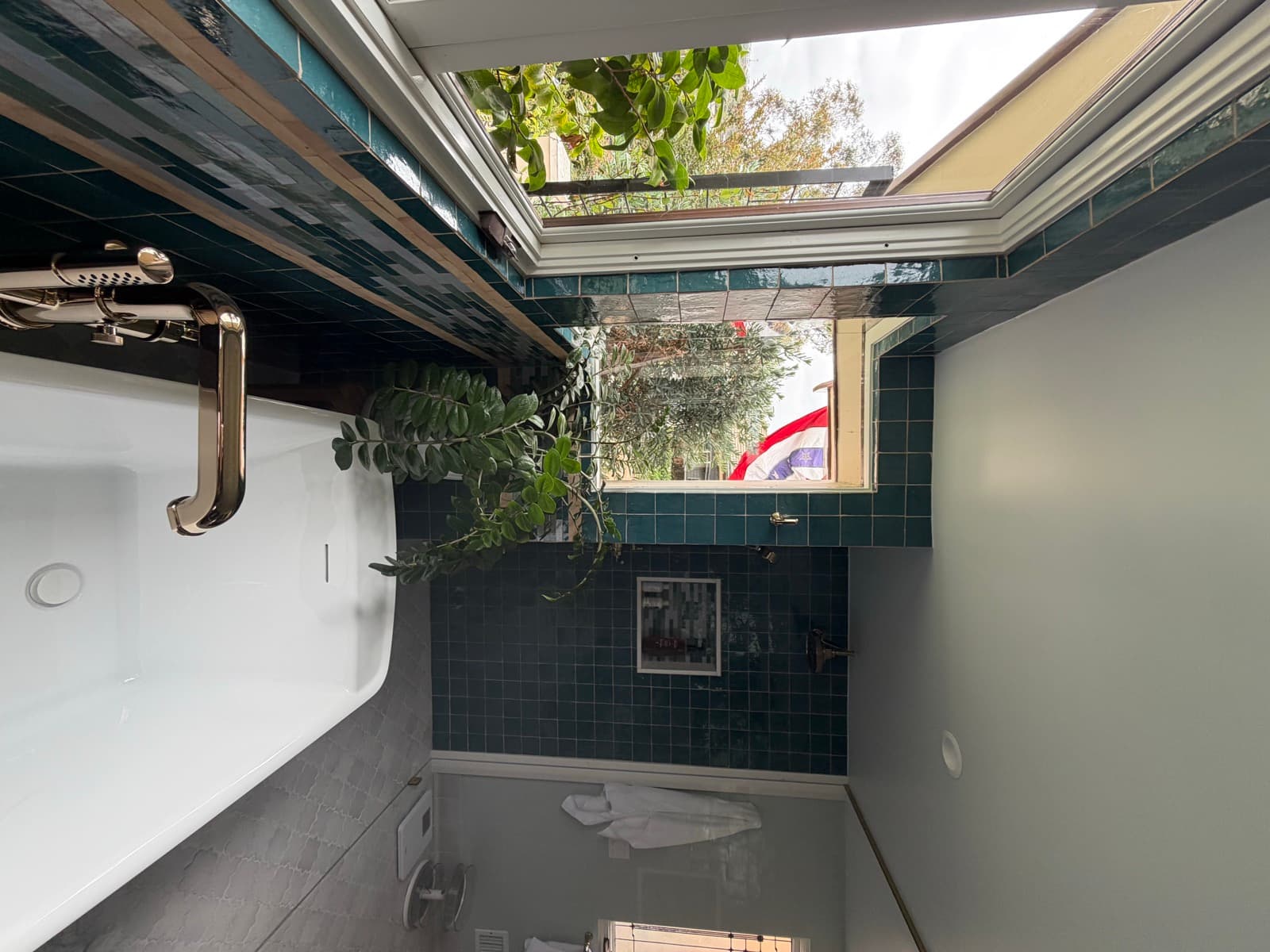 Freestanding tub and brass floor-mounted filler against teal tile, with garden windows on two sides