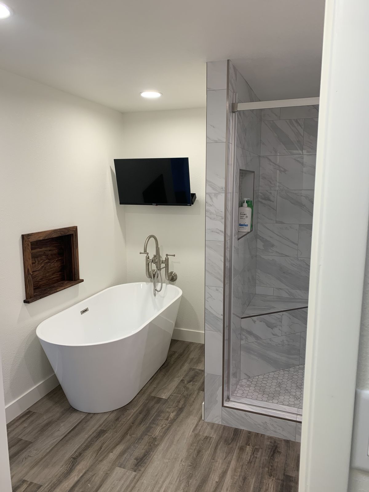 Freestanding soaking tub with floor-mounted filler beside the tiled shower